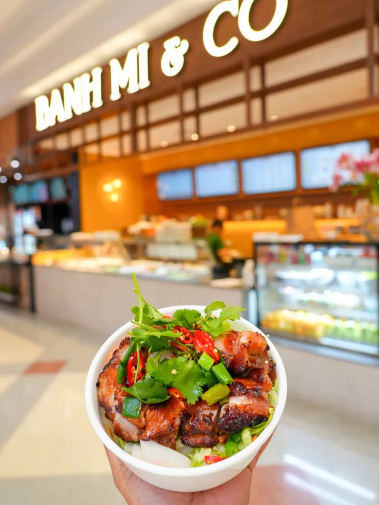 A chicken bowl held in front of the Banh Mi and Co shop sign at Winston Hills Mall