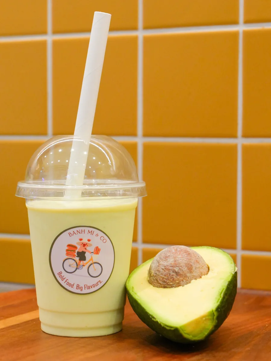 Avocado drink in a Banh Mi and Co cup beside a fresh avocado