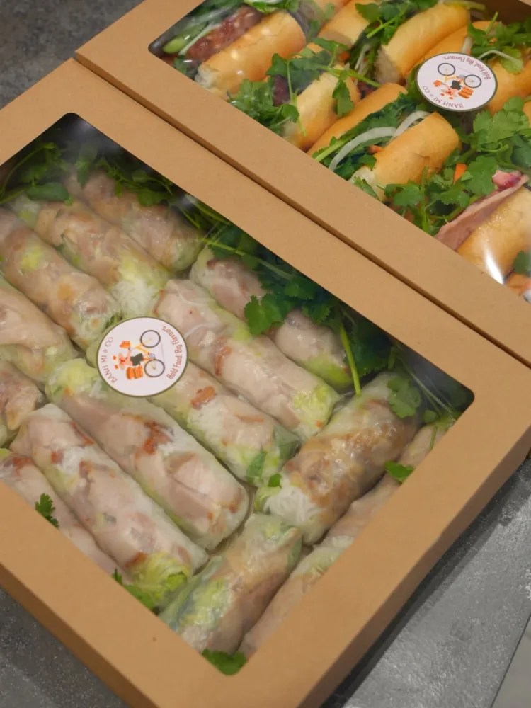 Boxed roast pork rice paper rolls alongside bánh mì catering